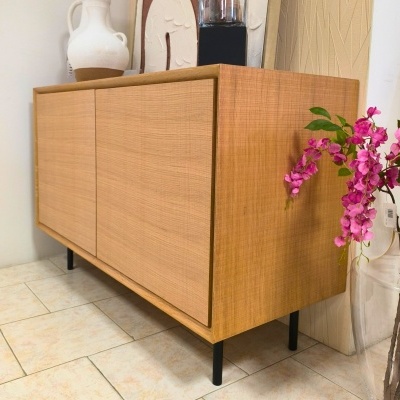 Aparador em madeira castanha clara com pernas pretas e flores cor-de-rosa ao lado