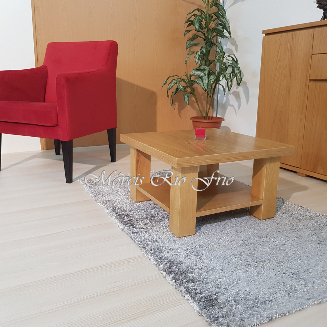 Mesa de centro de madeira clara com vela vermelha, cadeira vermelha, planta verde e móvel de madeira num ambiente interior.