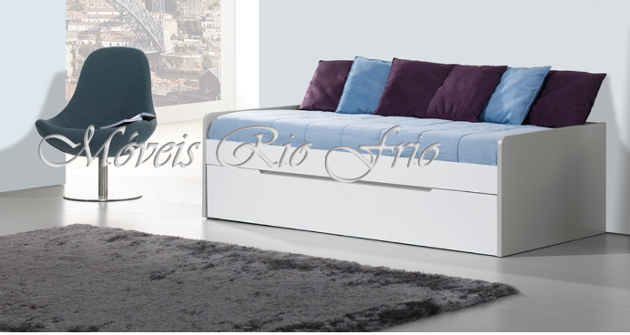 Sofá-cama branco com almofadas azuis e roxas num ambiente minimalista com cadeira azul e tapete cinzento