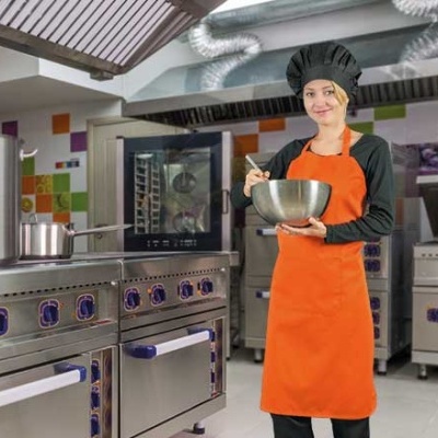 Cozinheira com avental laranja e chapéu preto em cozinha industrial