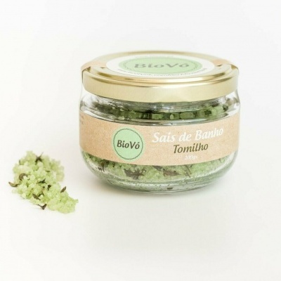Frasco de sais de banho com tomilho em vidro e tampa dourada, com ramo de tomilho ao lado.