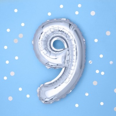 Balão prateado em forma do número 9 sobre fundo azul claro com confetes