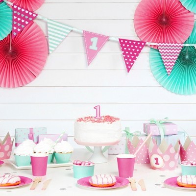 Mesa de festa de aniversário decorada com tons rosa e verde água, bolo com vela número 1, cupcakes e decoração pendurada