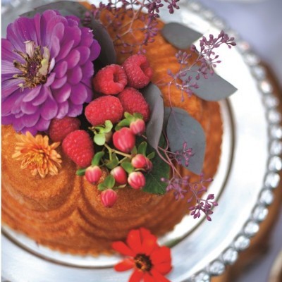 Bolo decorado com flores naturais e framboesas num prato prateado