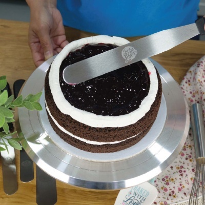 Bolo de chocolate com creme e geléia num prato giratório de metal com espátula.