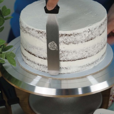 Bolo redondo de chocolate com creme branco em base metálica giratória com espátula