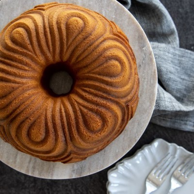 Bolo bundt dourado com padrão ondulado em prato de mármore claro