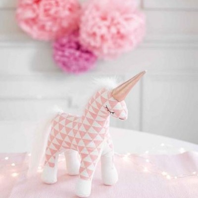 Pelúcia de unicórnio rosa com padrão geométrico e chifre dourado em ambiente decorado