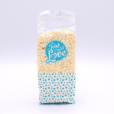 Pacote transparente com pequenos corações brancos e etiqueta azul com texto branco 'Just add Love'