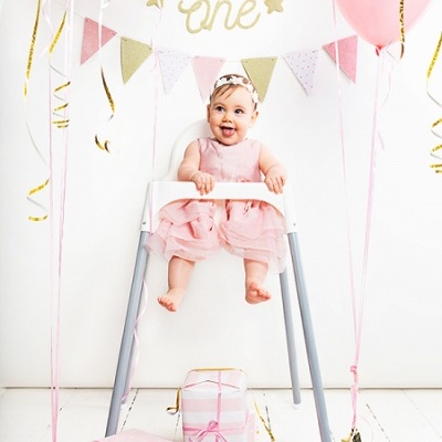 Criança sentada em cadeira alta branca com pernas cinza, balões e presentes rosa