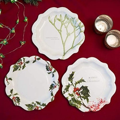 Três pratos decorativos festivos com motivos de azevinho, bagas e plantas verdes sobre fundo vermelho com velas e guirlanda de luzes.