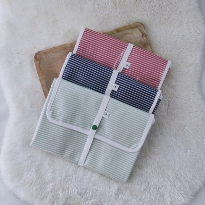 Três toalhas ou mantas riscas vermelhas, azuis e verdes claras dobradas sobre madeira e tapete branco