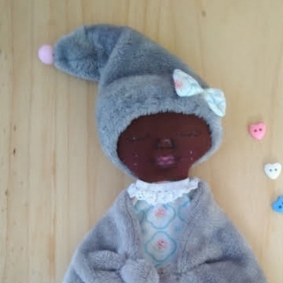 Boneca de tecido com roupa cinzenta felpuda e chapéu pontudo em fundo de madeira clara