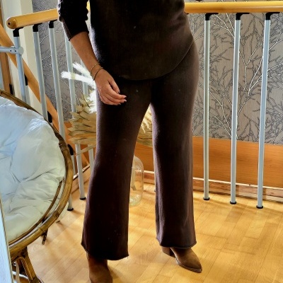 Conjunto castanho de malha com camisola de manga comprida e calças largas, botas castanhas, ambiente interior com chão de madeira.