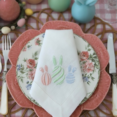 Mesa posta com prato rosa com padrão floral, guardanapo branco bordado e talheres