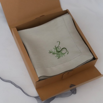 Guardanapo de tecido cinzento com bordado verde numa caixa de cartão castanho