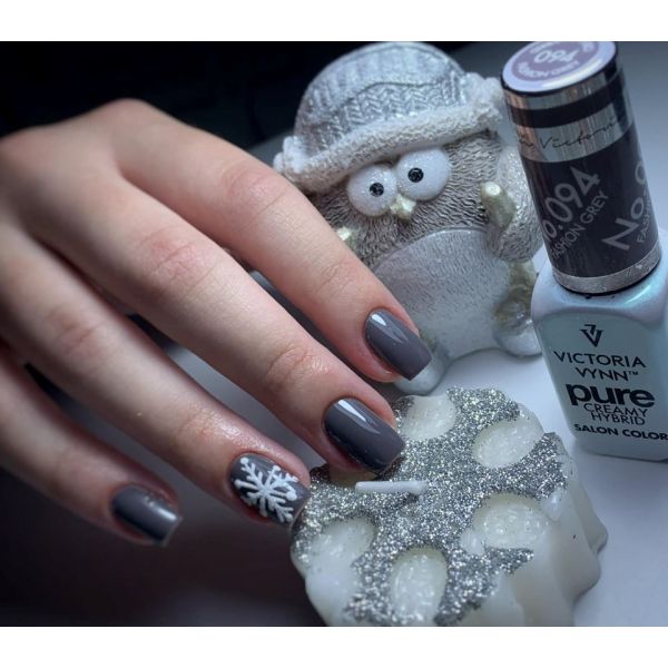 Unhas com verniz cinza escuro e desenho de floco de neve branco ao lado de vela decorativa e coruja de tecido.