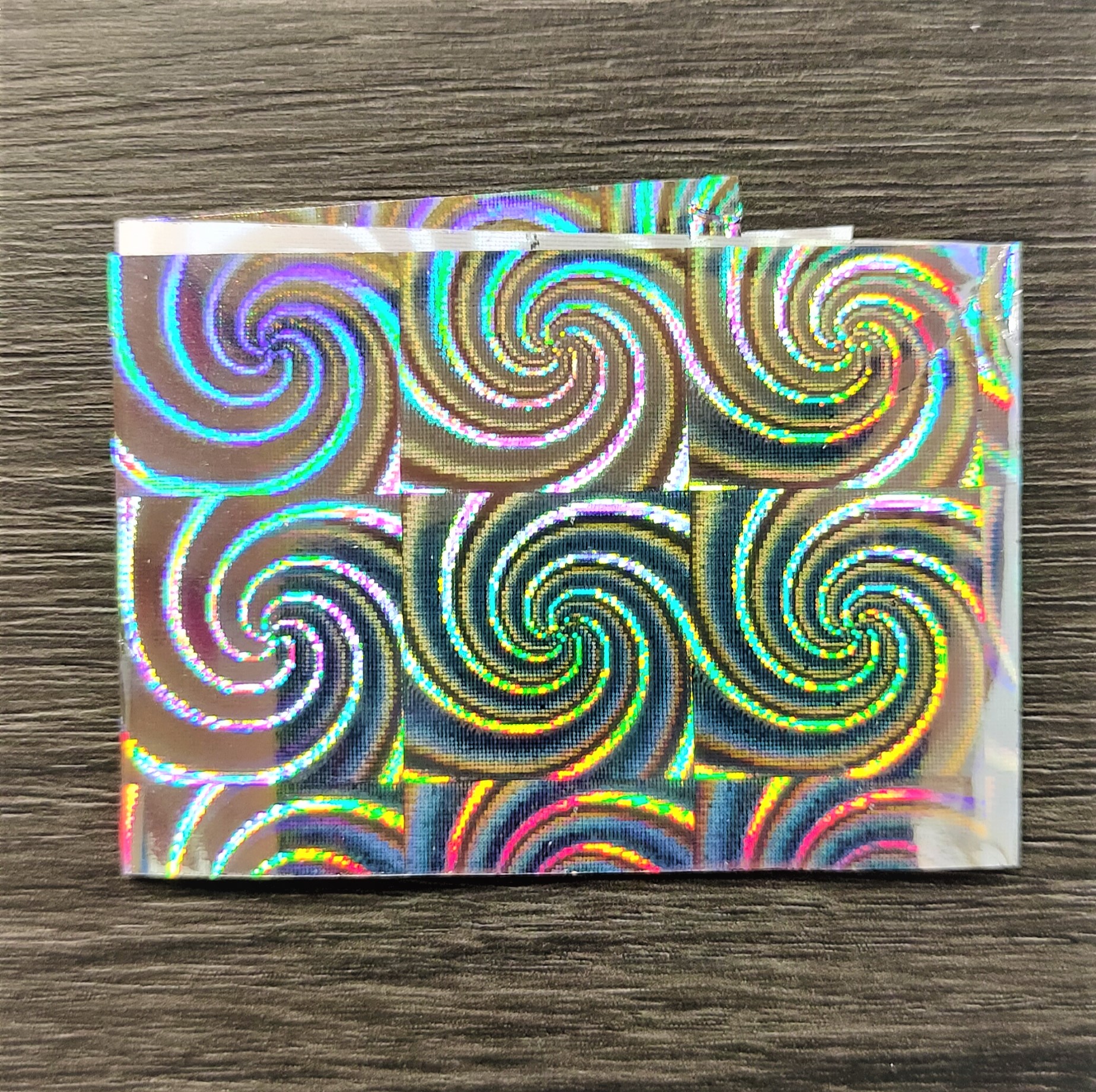 Folha holográfica com padrão de redemoinhos coloridos sobre madeira escura