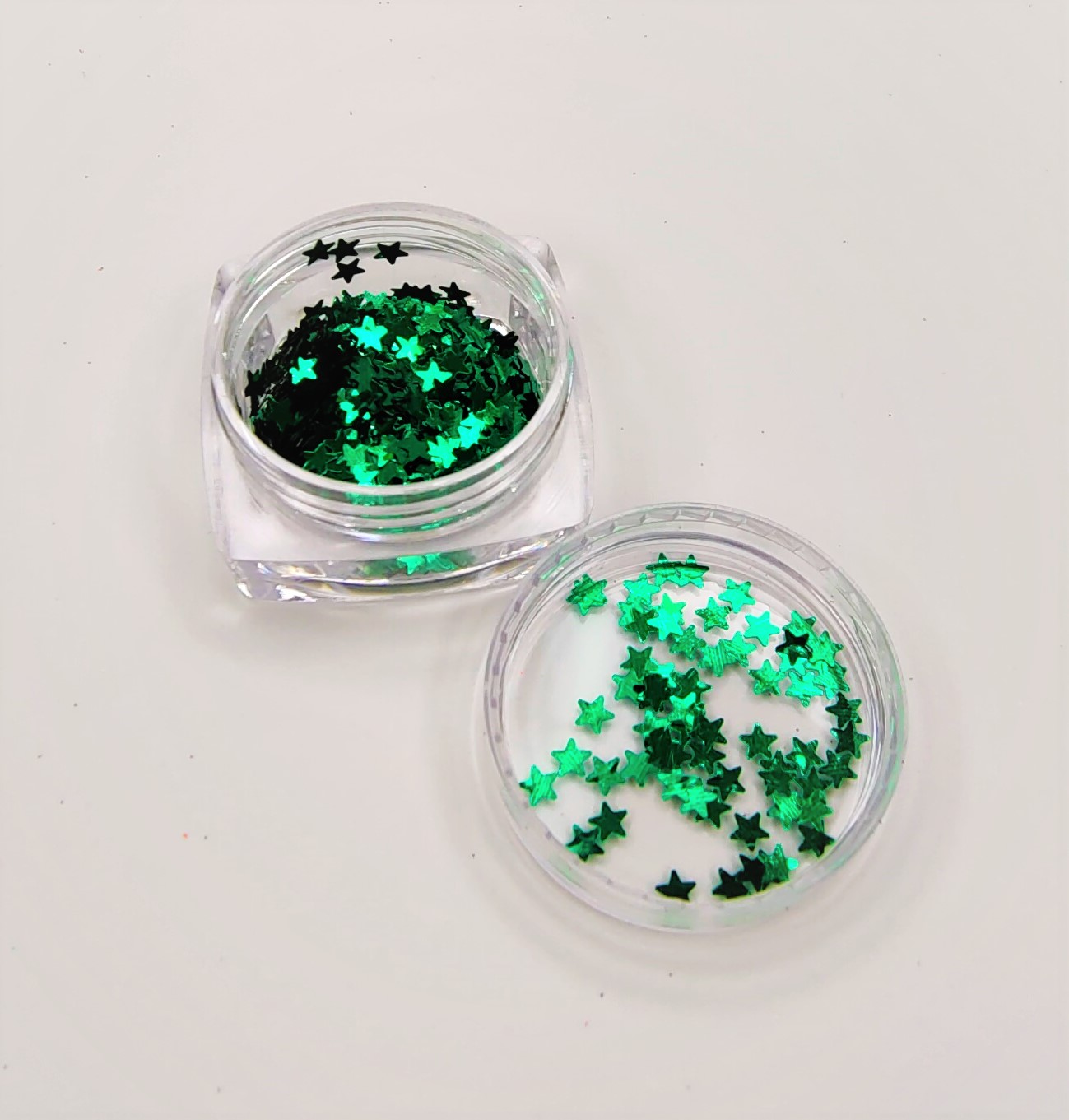 Purpurina em forma de estrelas verdes num recipiente de plástico transparente aberto sobre fundo branco.