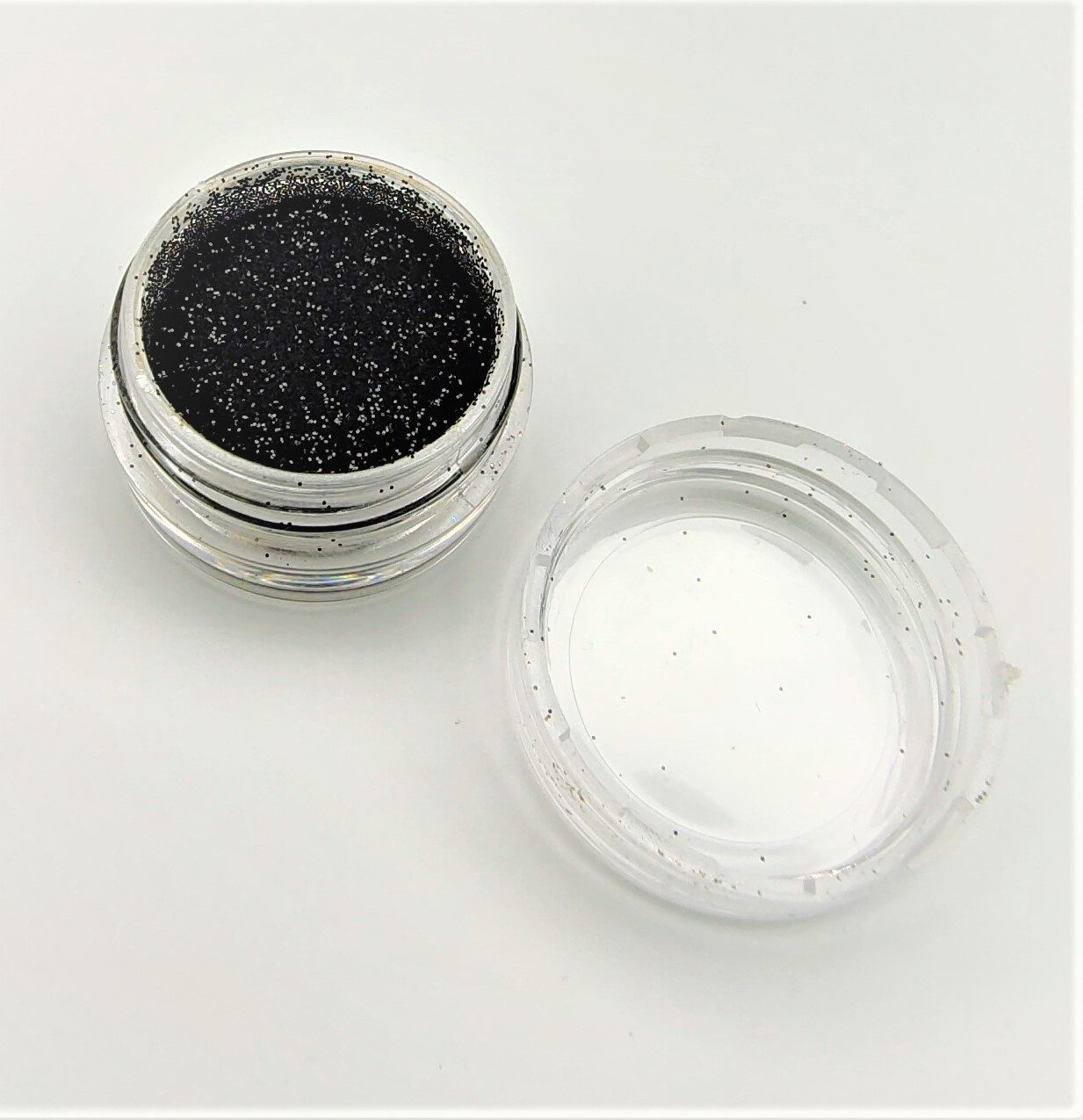 Pote pequeno com produto preto brilhante e tampa transparente ao lado