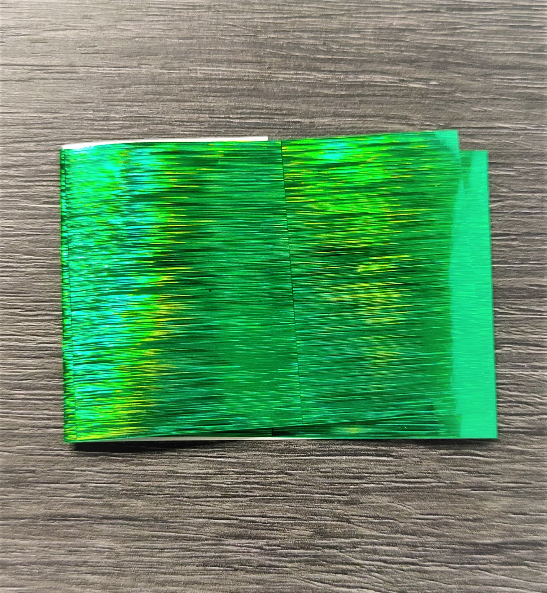 Folha de papel plástico holográfico verde sobre madeira cinzenta