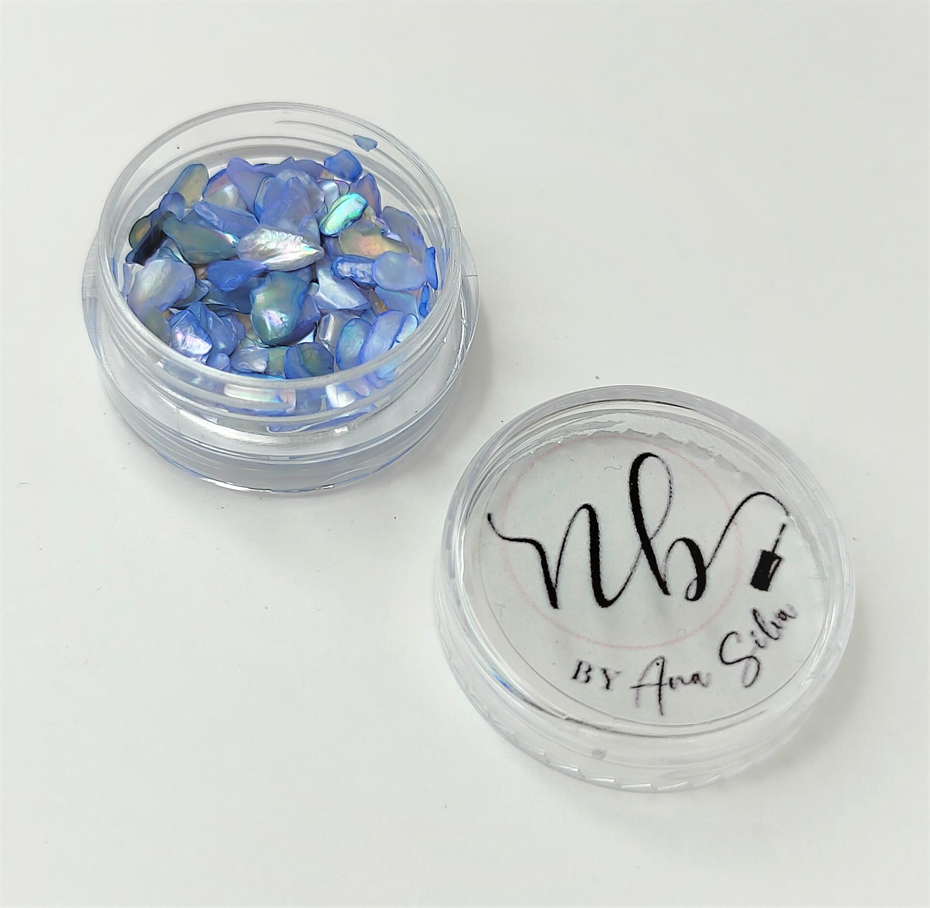 Frasco transparente com pedaços de concha azul e tampa com texto 'nb BY Ana Silva'.