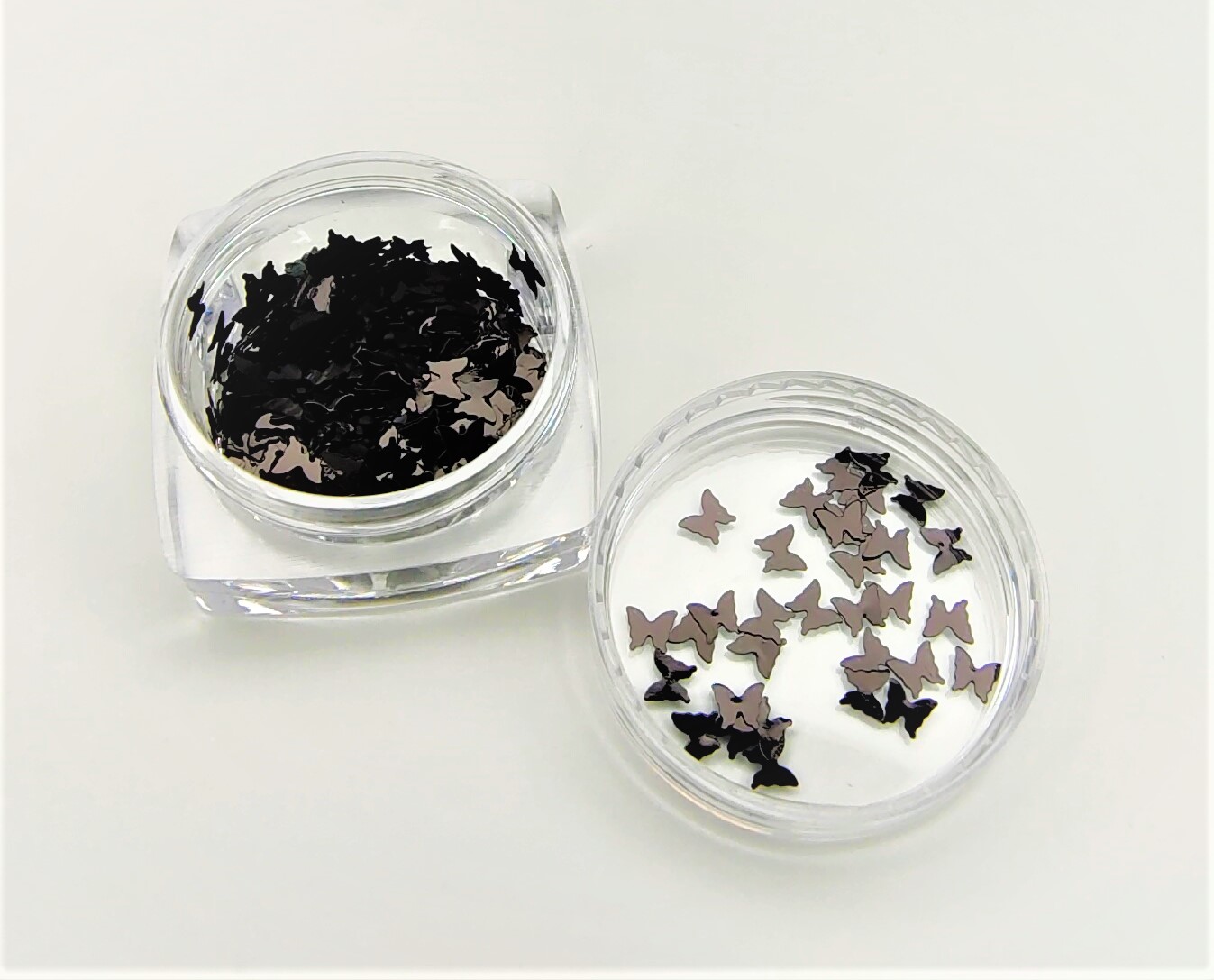 Frascos com pequenas figuras metálicas em forma de borboletas pretas e prateadas