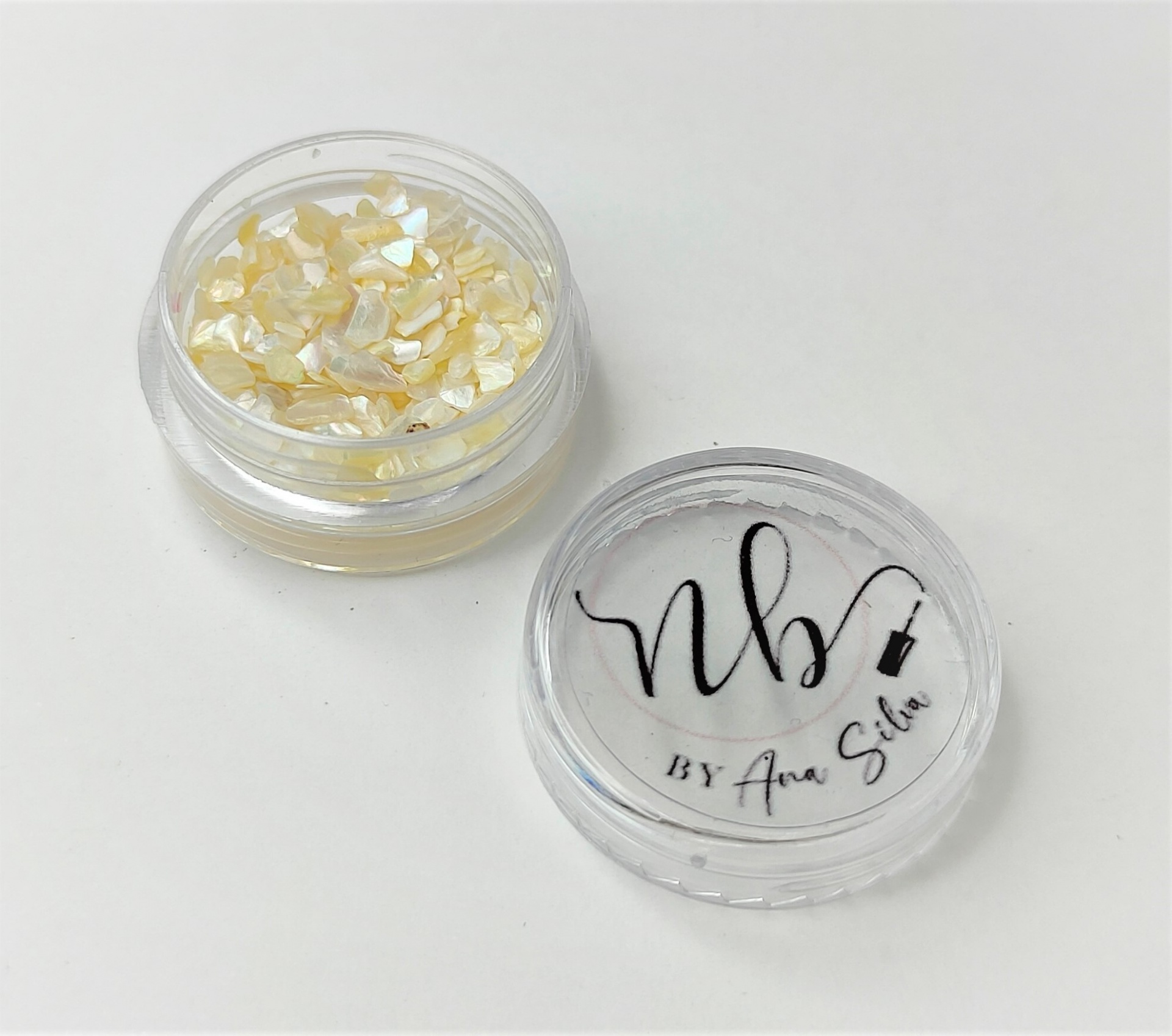 Pote transparente com pigmento perolado amarelo claro e tampa com texto preto 'nb BY Ana Silva'