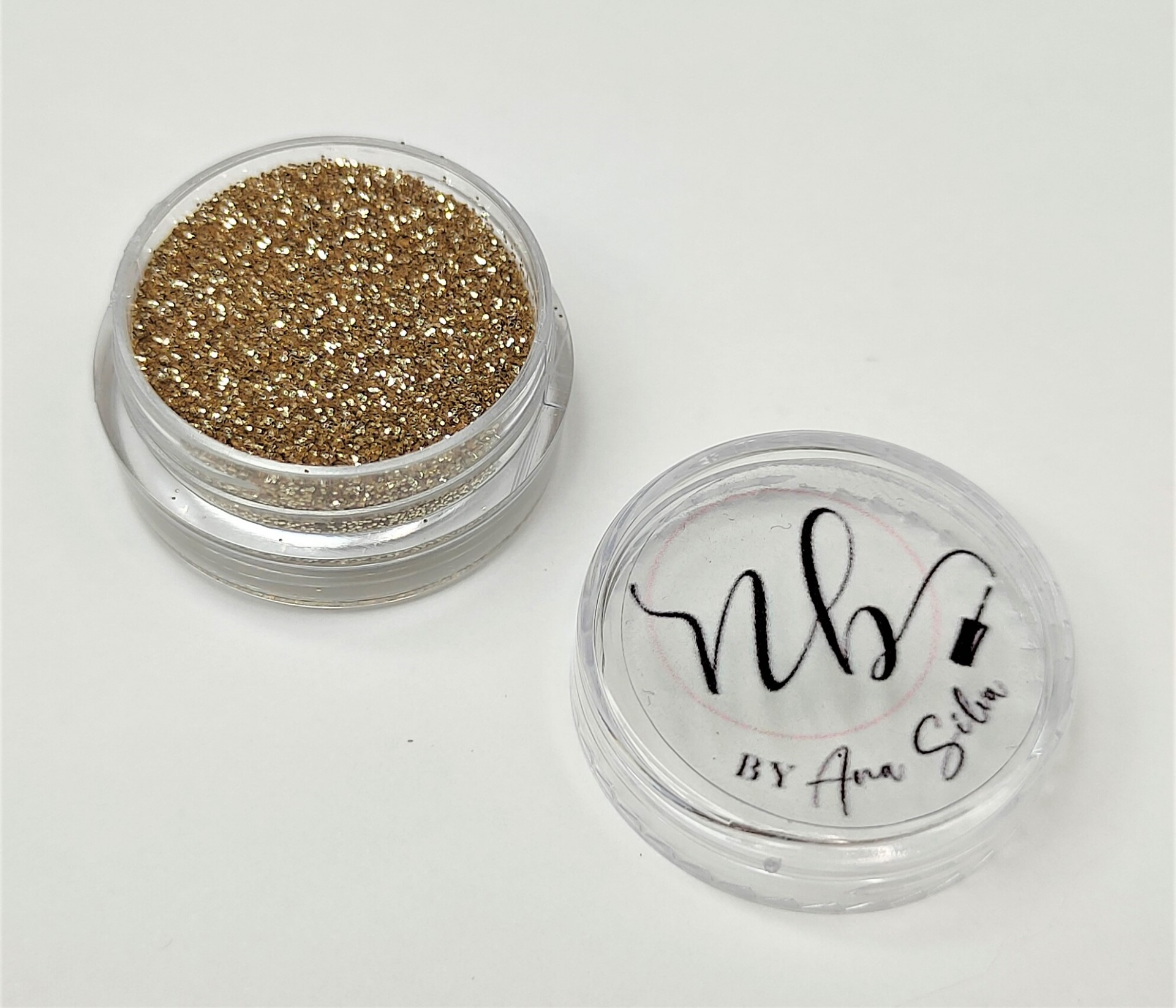 Pó glitter dourado em recipiente com tampa transparente com texto 'nb BY Ana Silva'