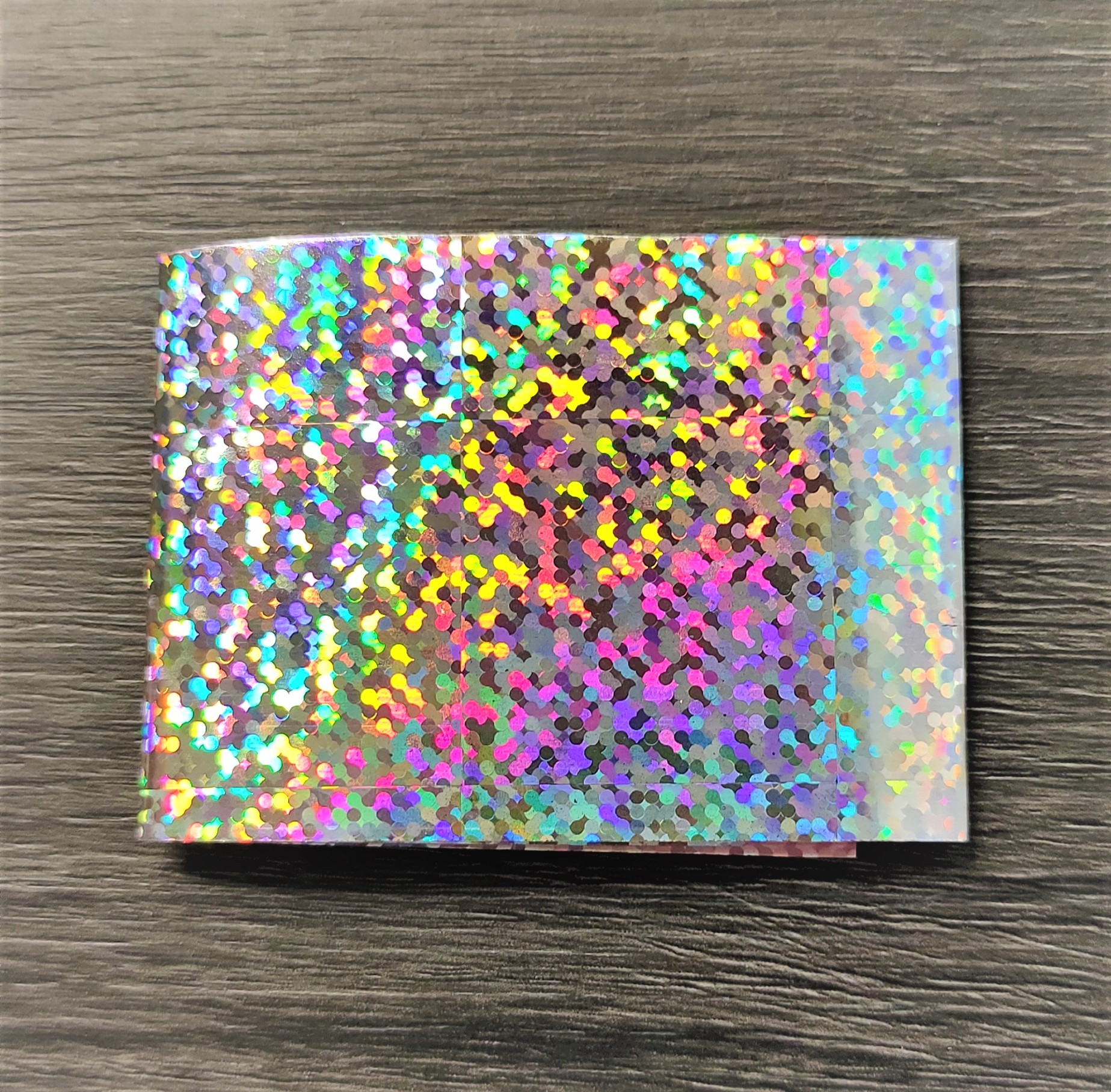 Folha de papel holográfico com padrão de pontos coloridos sobre madeira escura