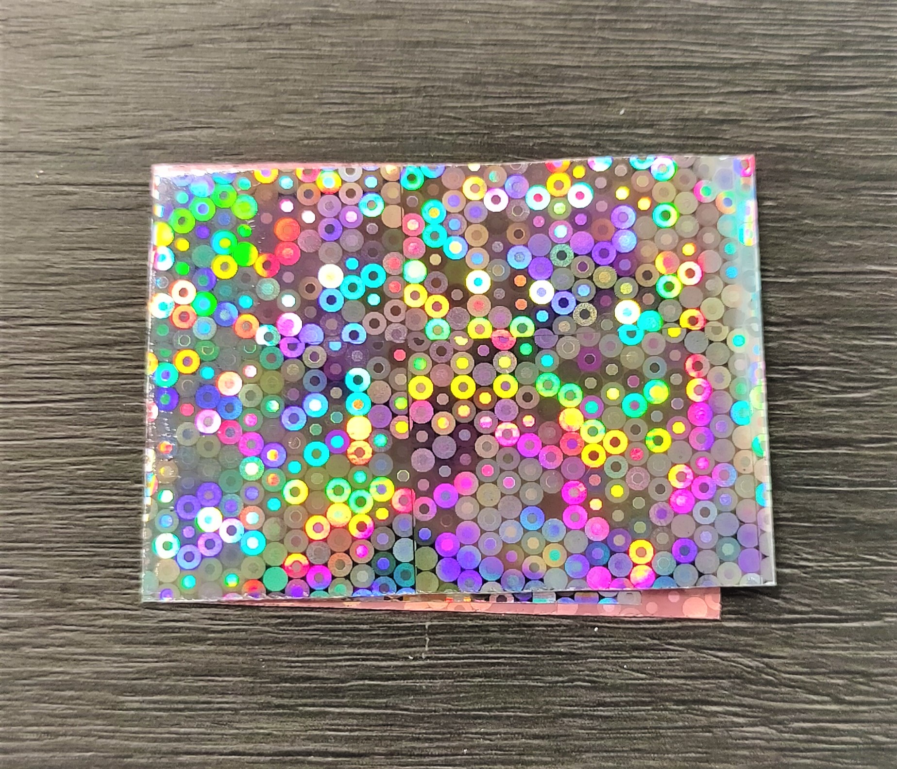 Cartão holográfico com círculos coloridos sobre fundo de madeira cinzenta