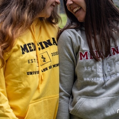 Duas pessoas com sweatshirts às cores amarela e cinza com texto universitário estampado