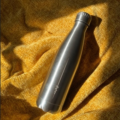 Garrafa térmica metálica prateada sobre tecido amarelo