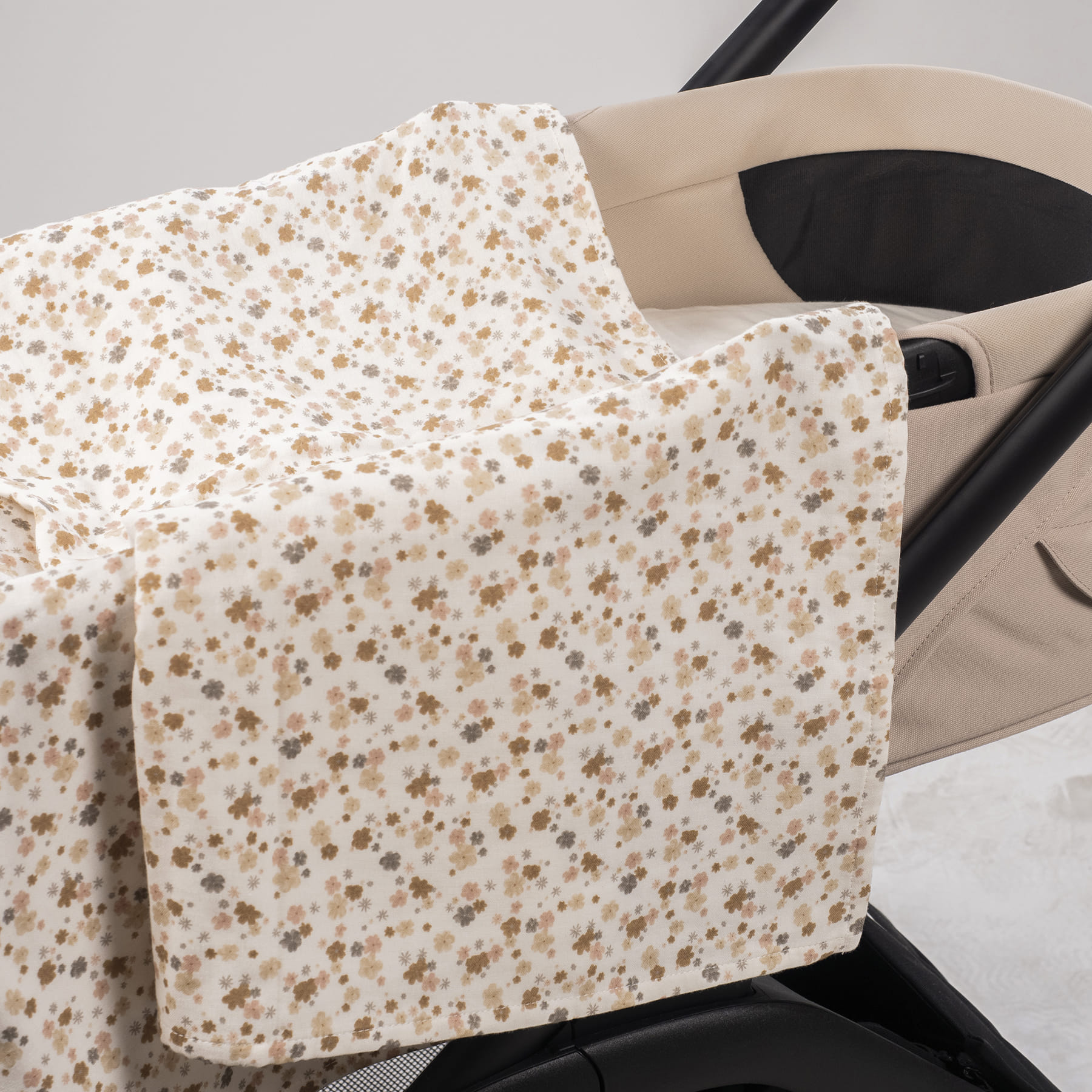 Cobertor com padrão floral bege e castanho sobre carrinho de bebé bege