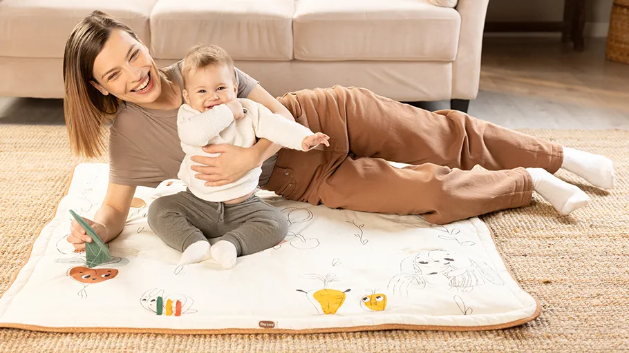 Mulher e bebé sobre tapete com ilustrações em sala de estar