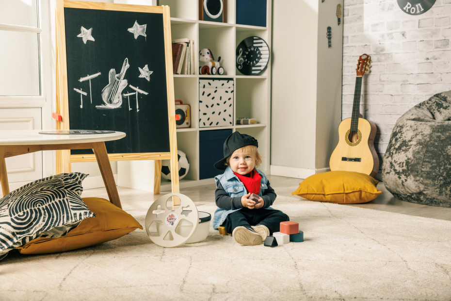 Criança a brincar com blocos de construção perto de um quadro negro e de um violão.