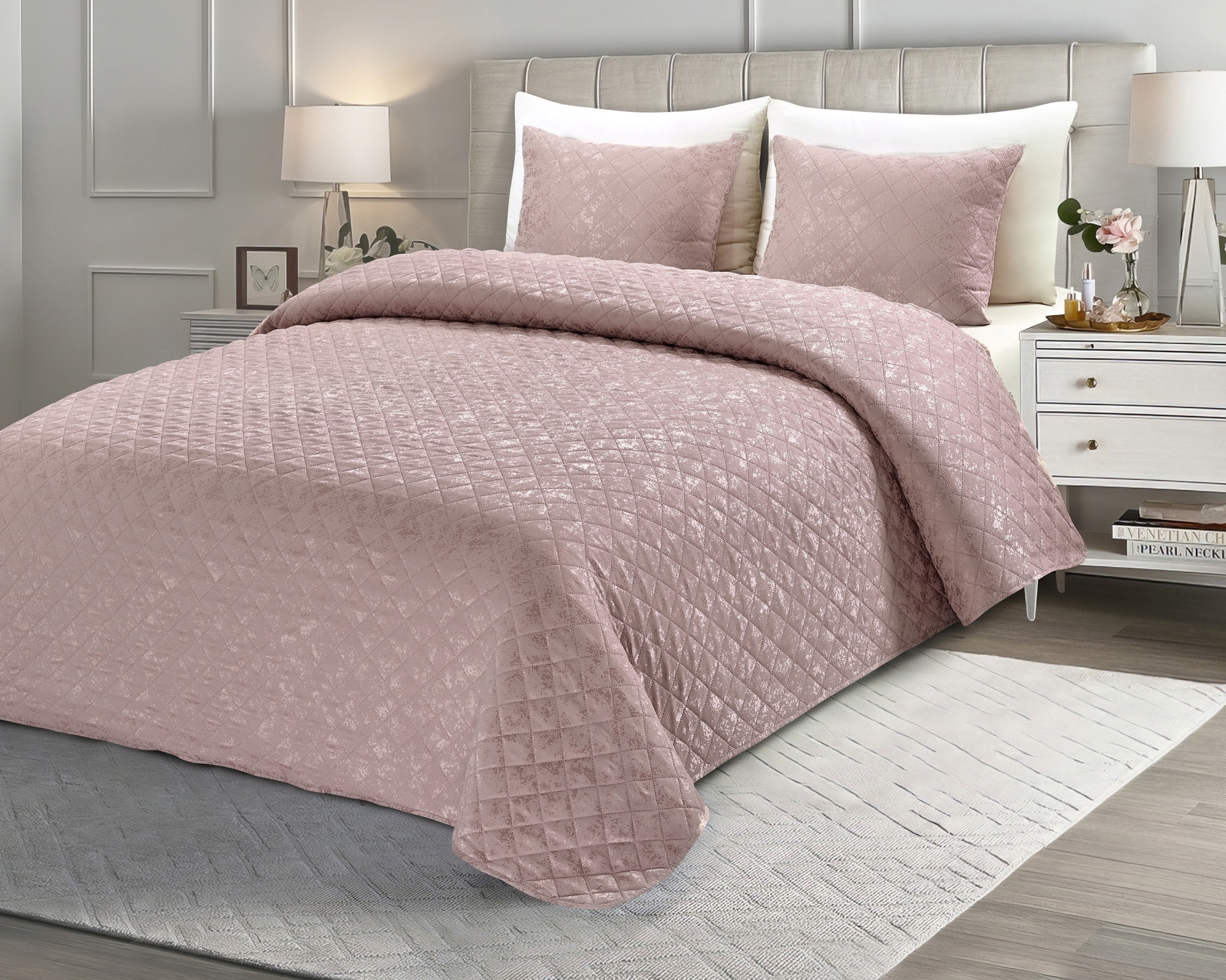 Colcha rosa claro com padrão de losangos numa cama estofada clara, com almofadas, mesas de cabeceira e candeeiros.