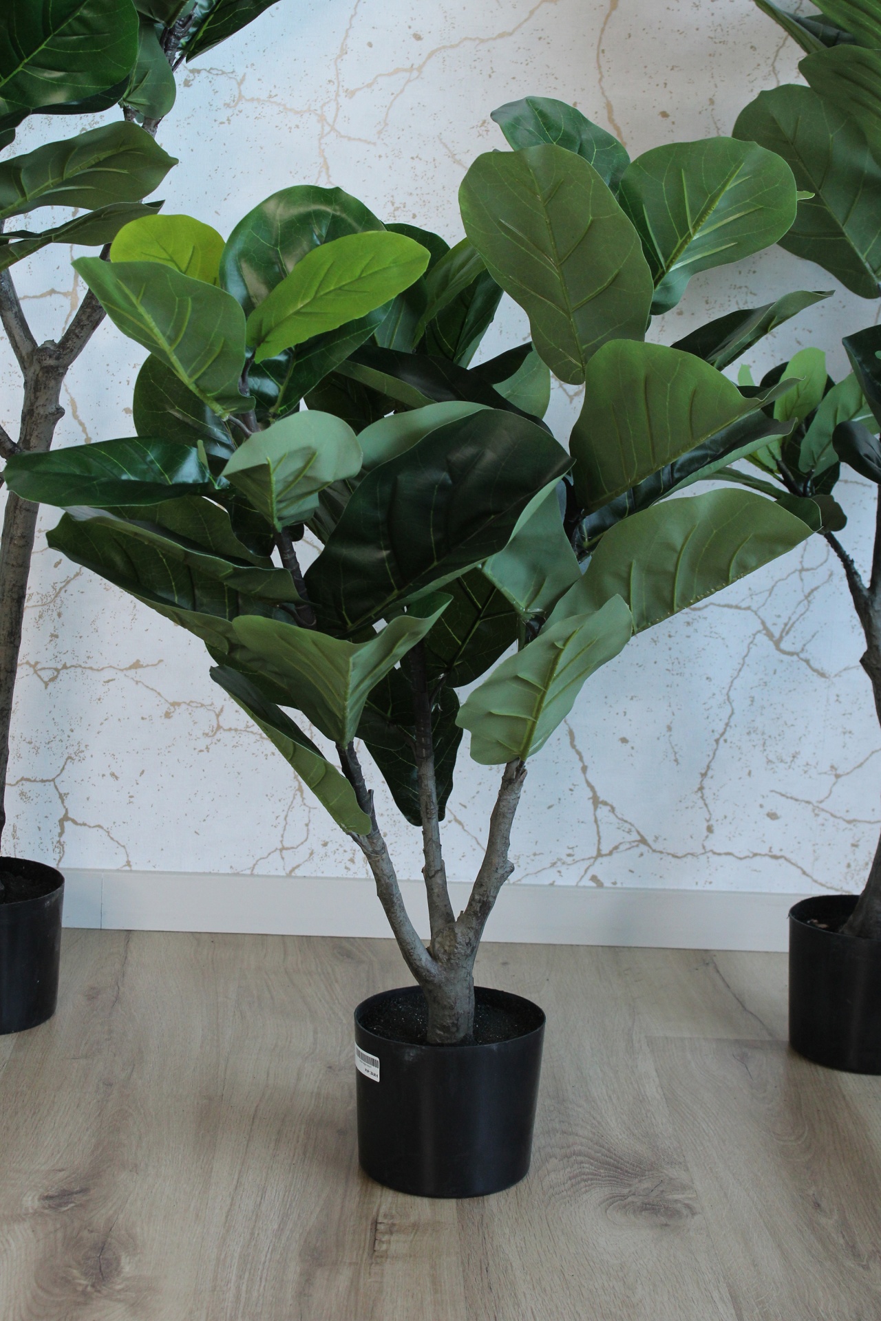 Planta artificial em vaso preto com folhas verdes largas