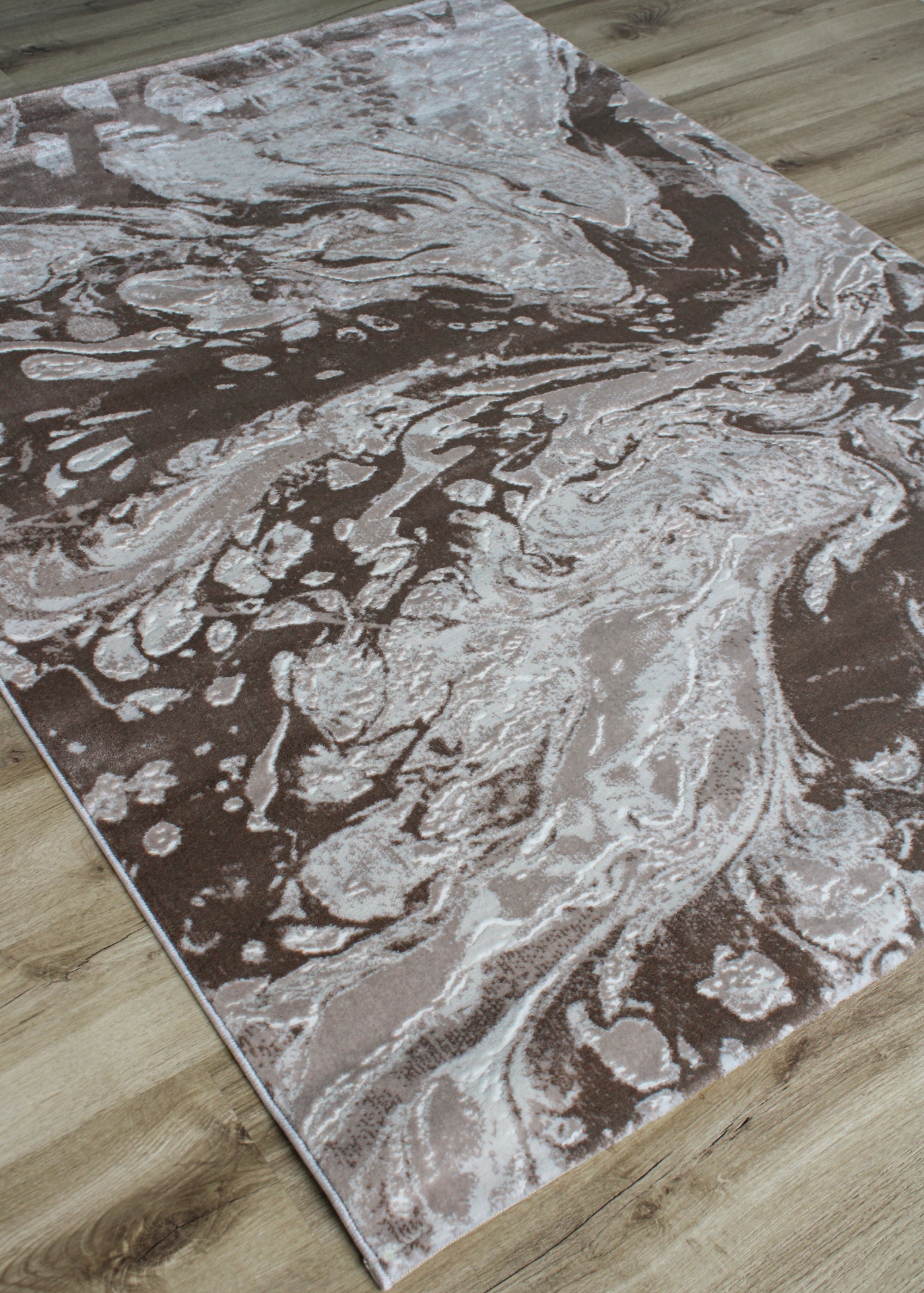 Tapete com padrão abstracto em castanho, bege e branco sobre chão de madeira.