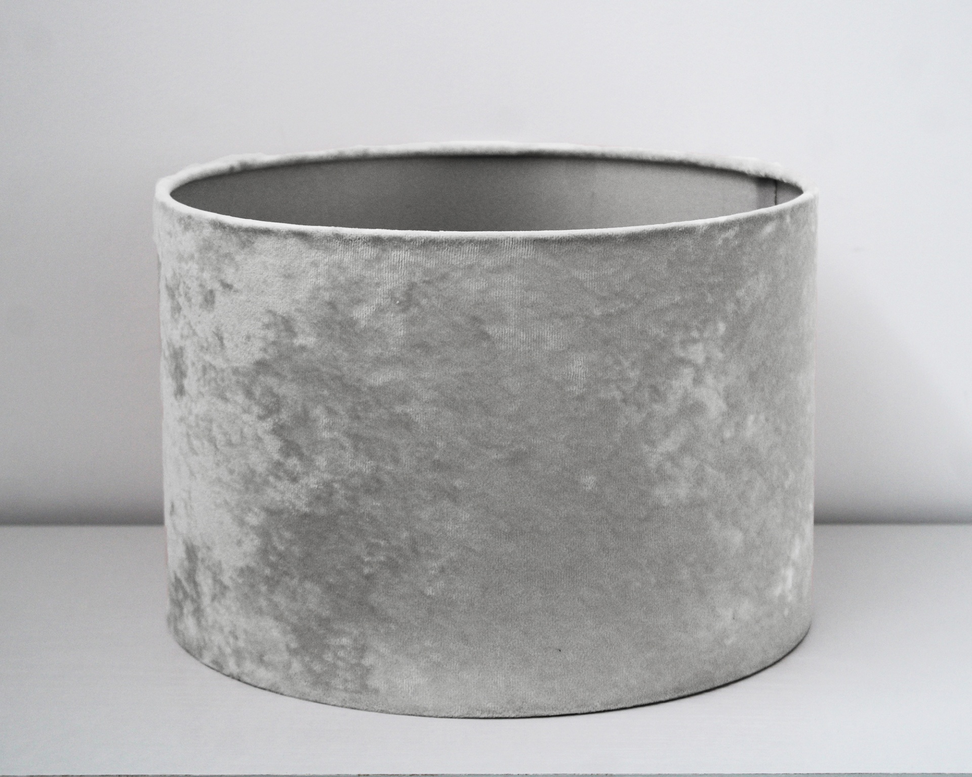 Abajur cylindrical cinzento de veludo amassado sobre superfície branca