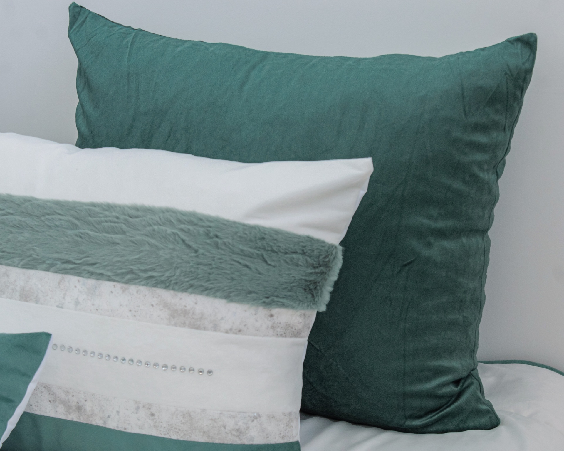 Três almofadas com diferentes texturas e cores sobre cama branca