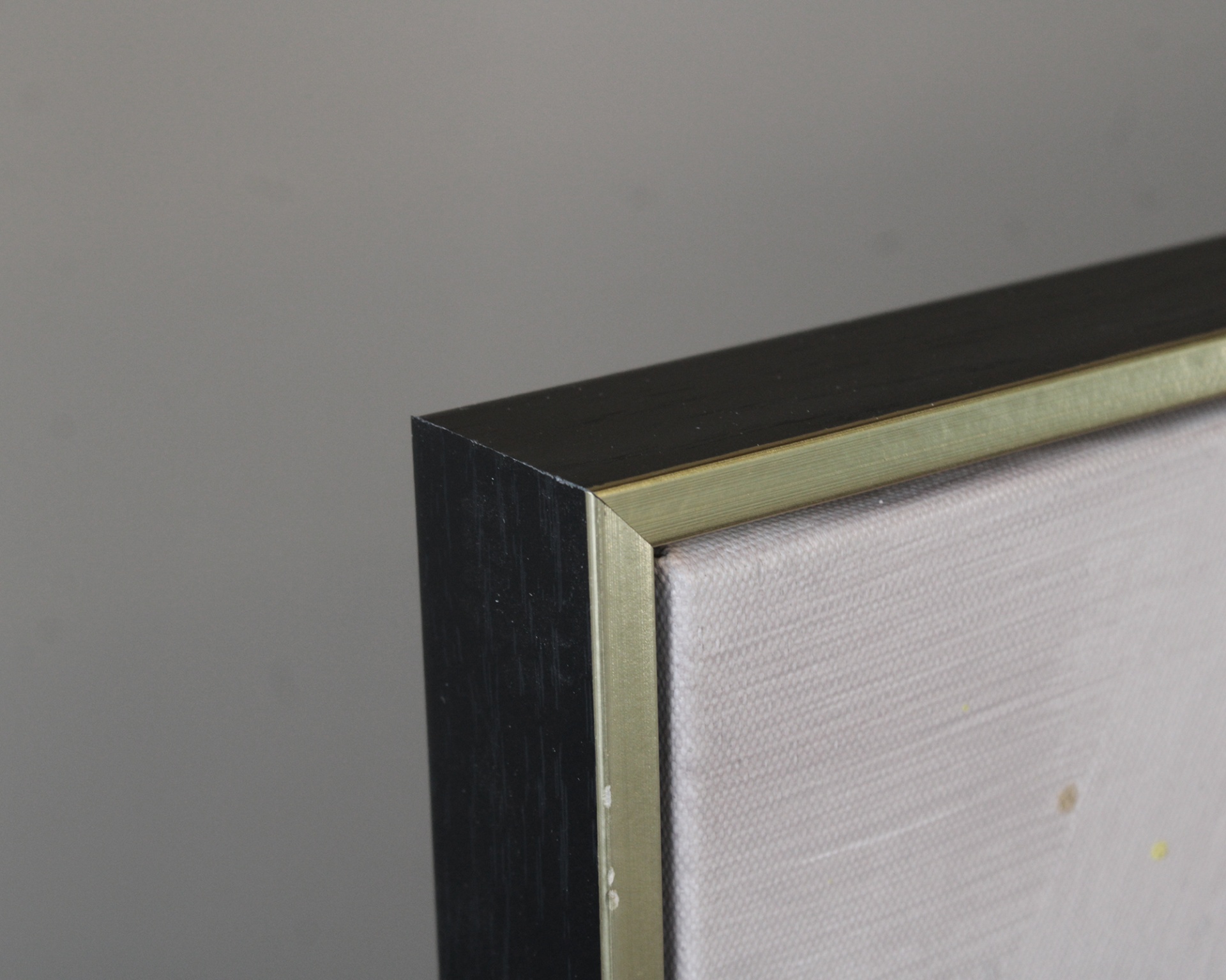 Canto de moldura preta com acabamento dourado e tela branca com manchas.