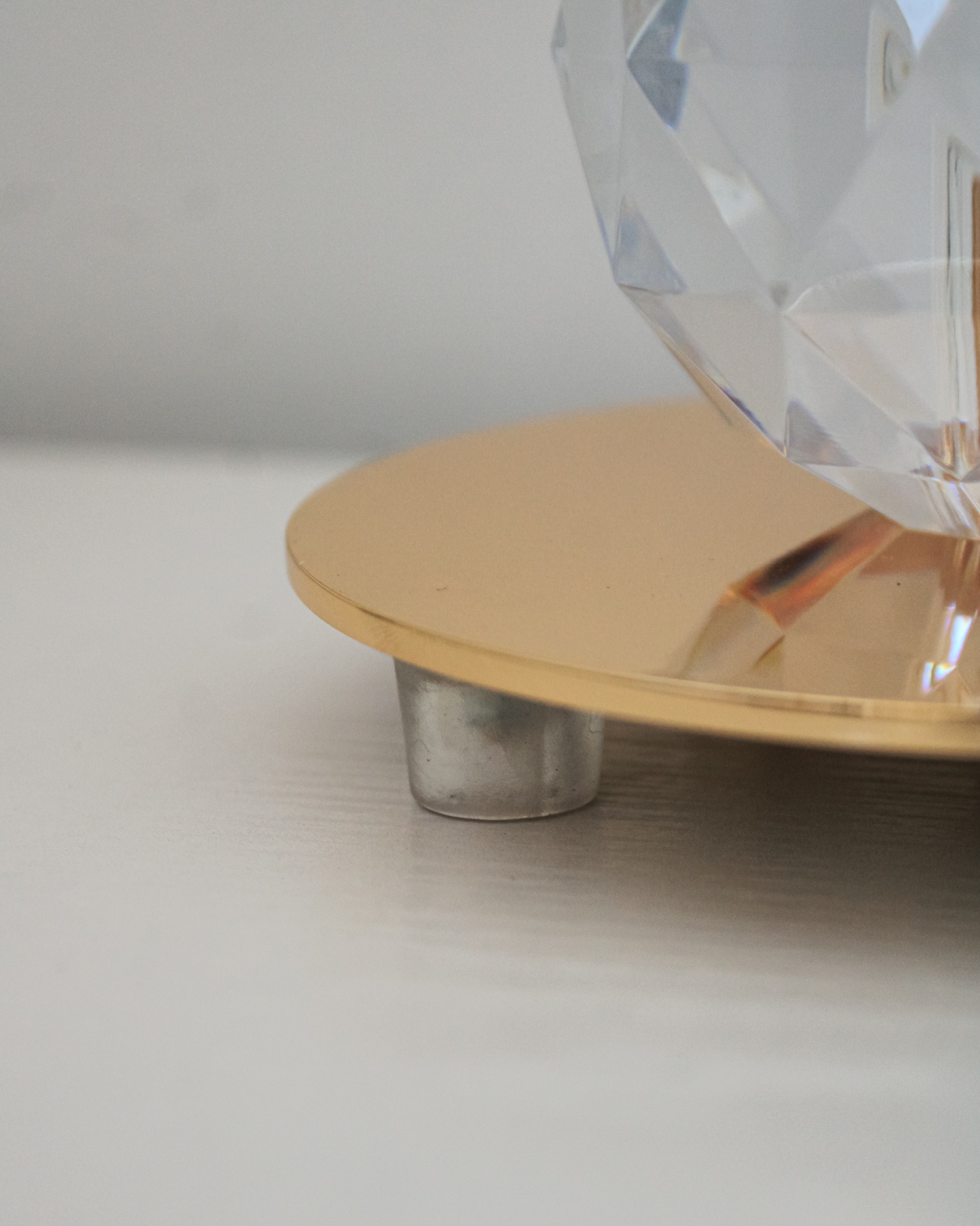 Base dourada metálica com apoio cinzento e objeto facetado transparente