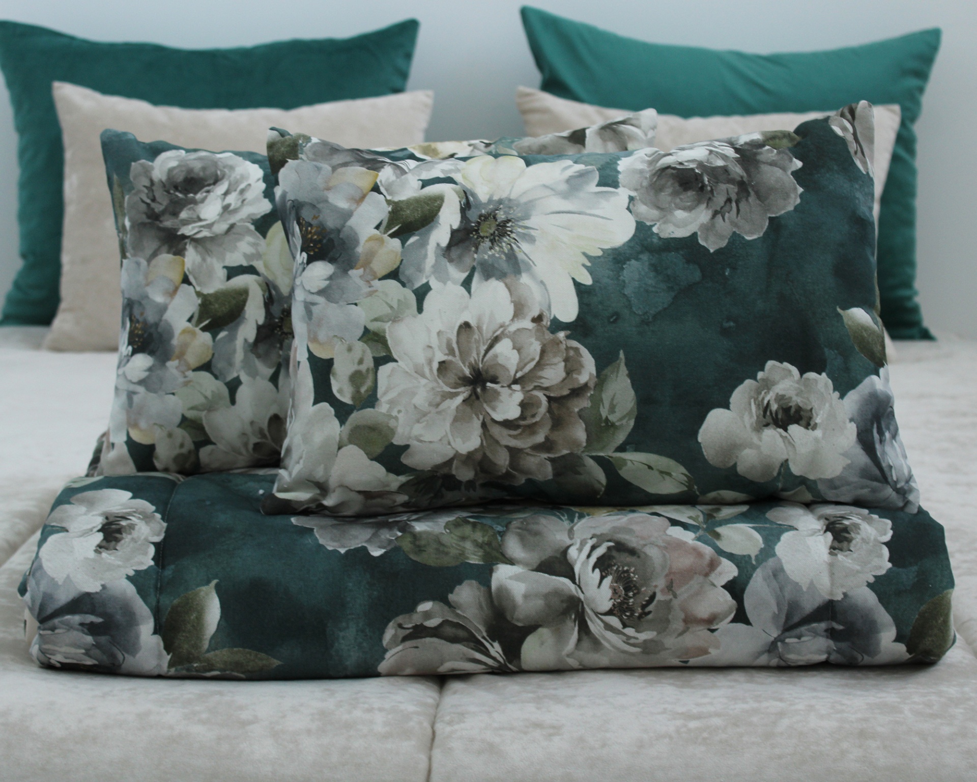 Almofadas e manta com padrão floral verde e branco sobre cama com almofadas lisas