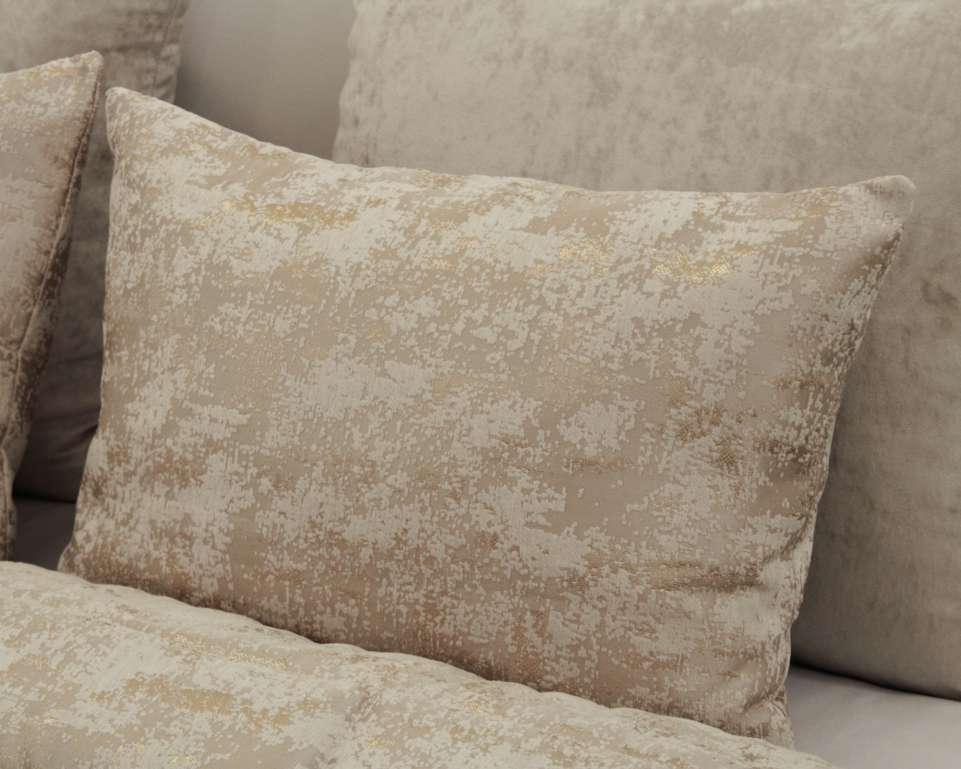 Almofada decorativa bege com padrão dourado sobre sofá neutro