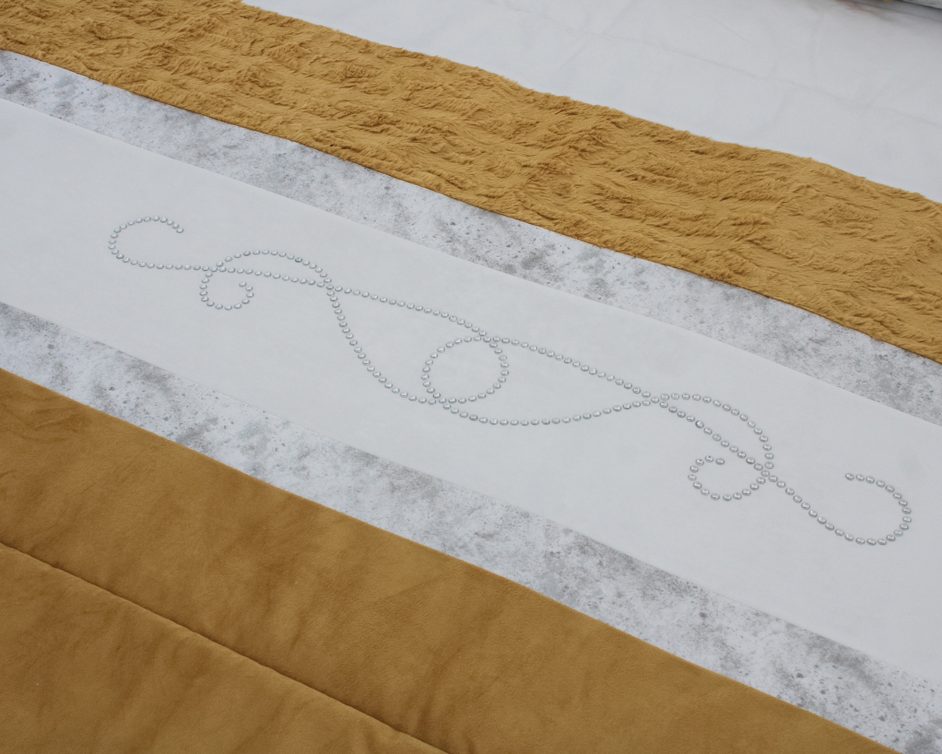 Colcha de cama castanha, bege e branca com padrão decorativo de pontos na faixa central