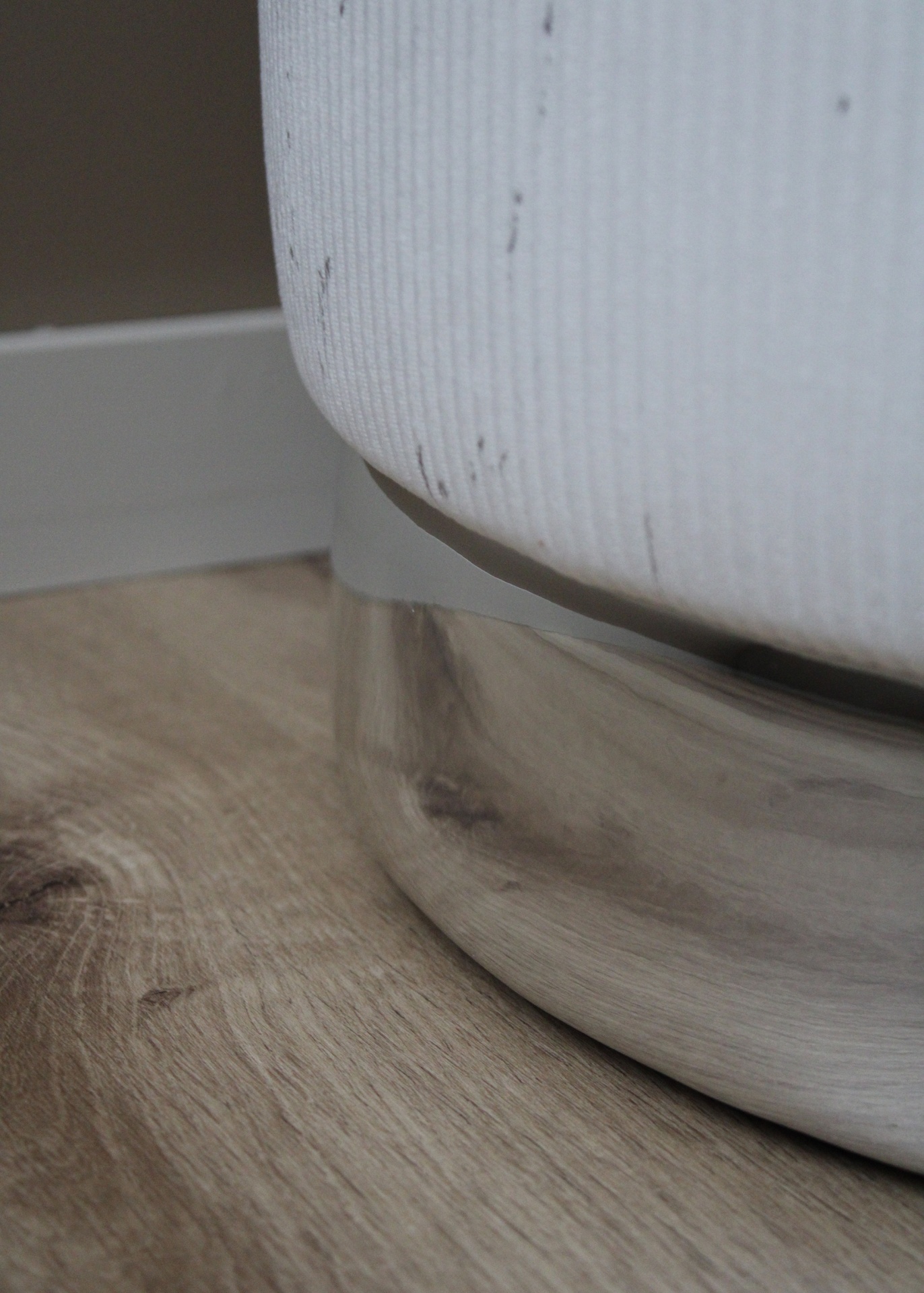 Base metálica prateada e tecido branco de móvel estofado sobre chão em madeira