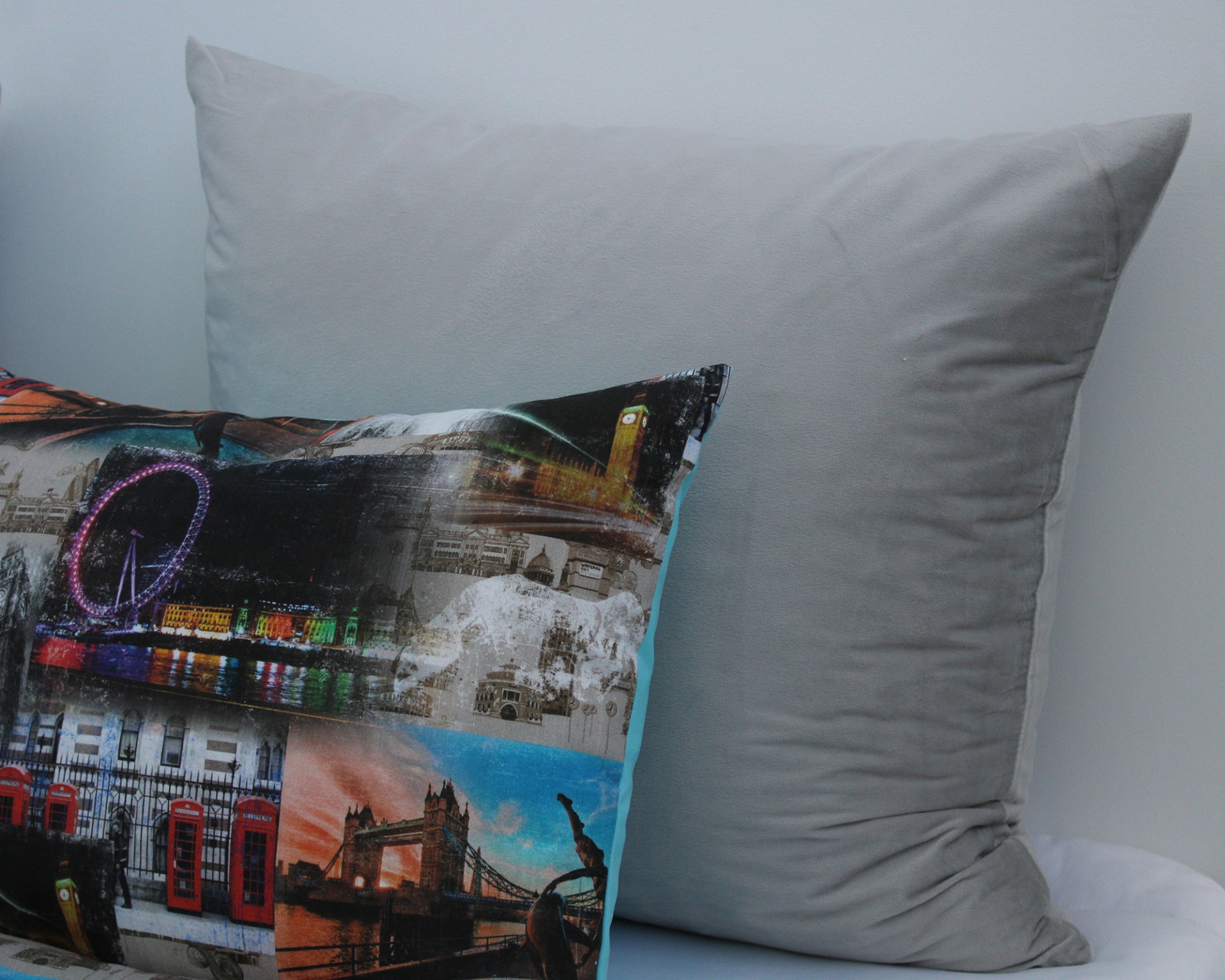 Almofadas decorativas, uma com estampas urbanas coloridas e outra cinza lisa