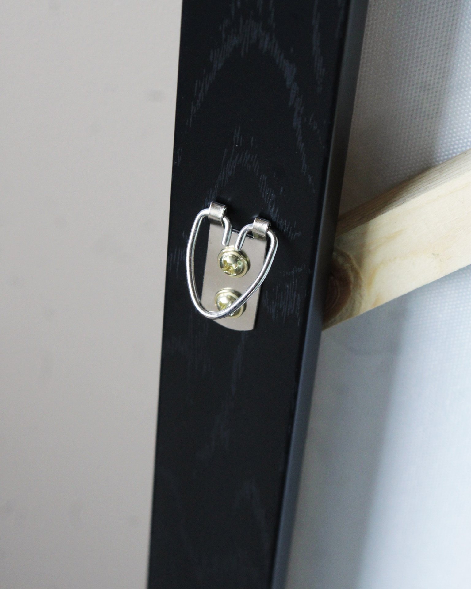 Gancho metálico prateado numa moldura de madeira preta com superfície clara de madeira e tela ao fundo