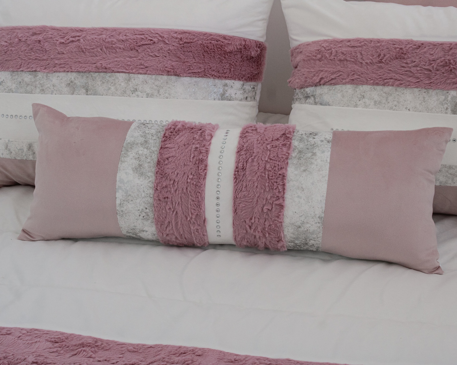 Conjunto de almofadas decorativas rosas e cinza com textura e pedraria sobre cama branca